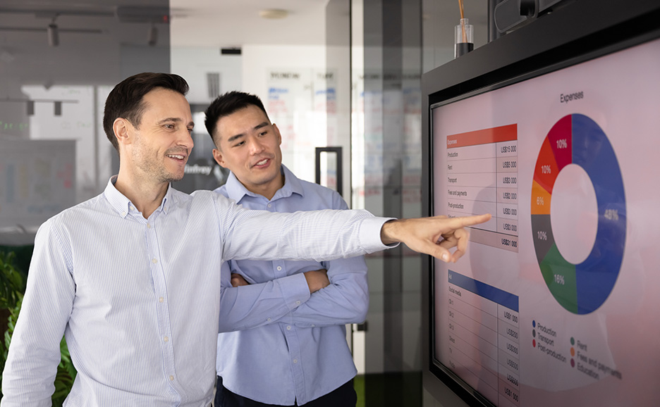 Two men pointing at a graph displayed on a screen