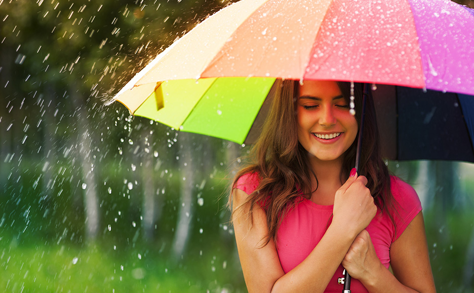 A smiling woman walking in the rain with a colorful umbrella
