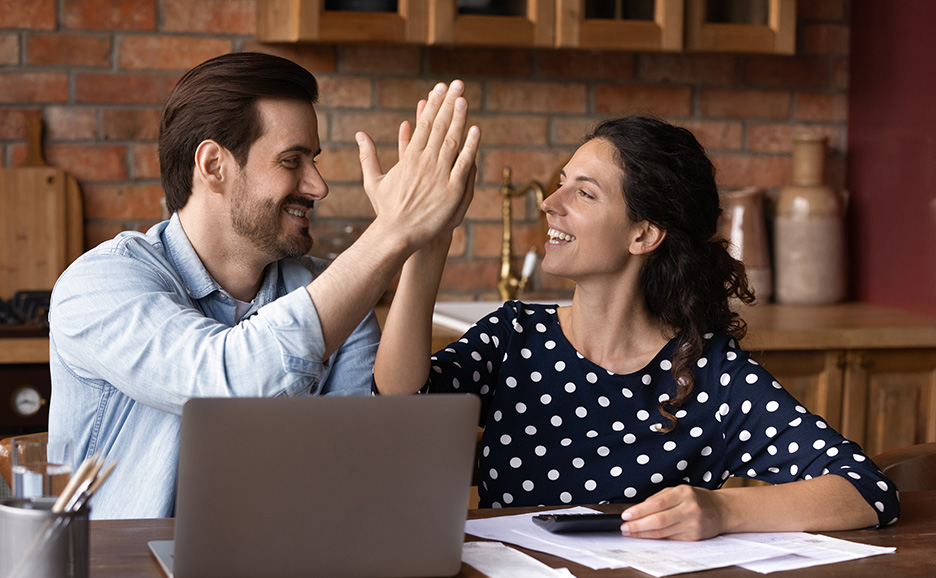 A smiling couple high-fiving while looking at a laptop at home