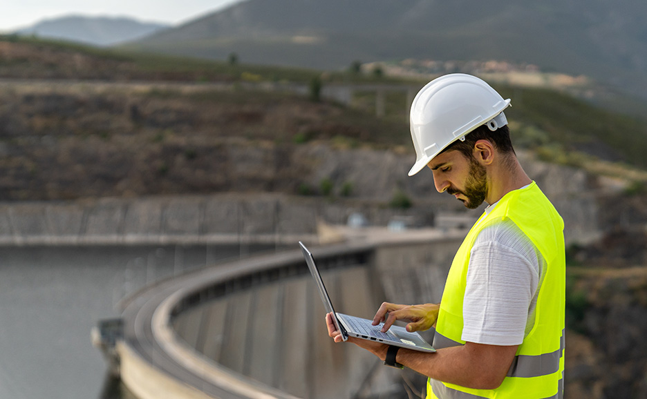 ノートPCを片手にダムの確認をしている作業員