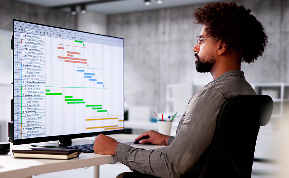 机でコンピューターモニターのガントチャートを分析する男性