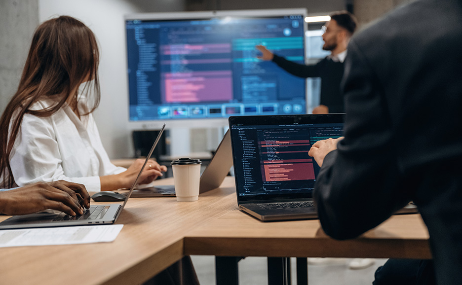 プログラミングコードが表示された画面を囲む開発チーム