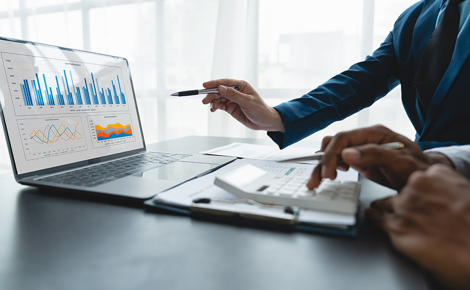 Business professional pointing to graphs on a laptop and another person using a calculator
