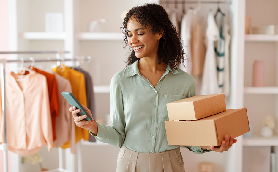 荷物を持ってスマートフォンを操作しながら微笑む女性