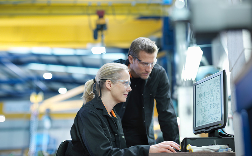 Man and woman reviewing blueprints on a computer in a manufacturing plant