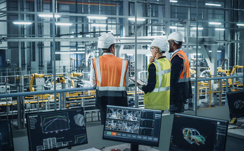 Three people overlooking a factory production line and conversing