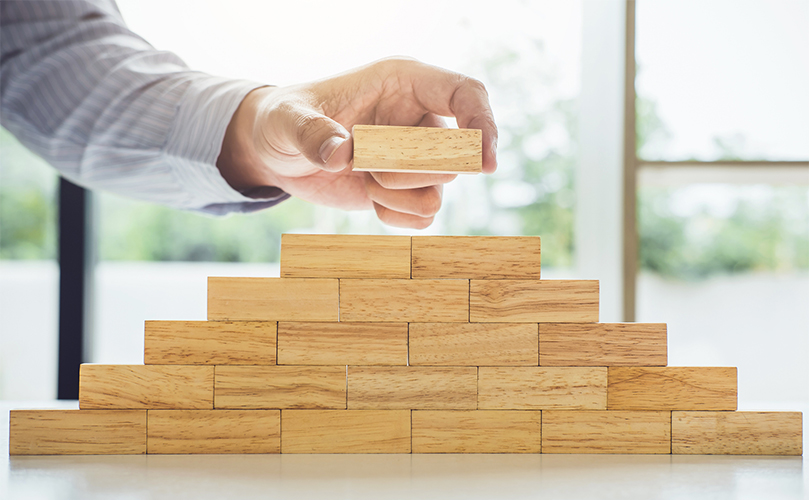 A hand places a wooden block on top of a tower of wooden blocks.
