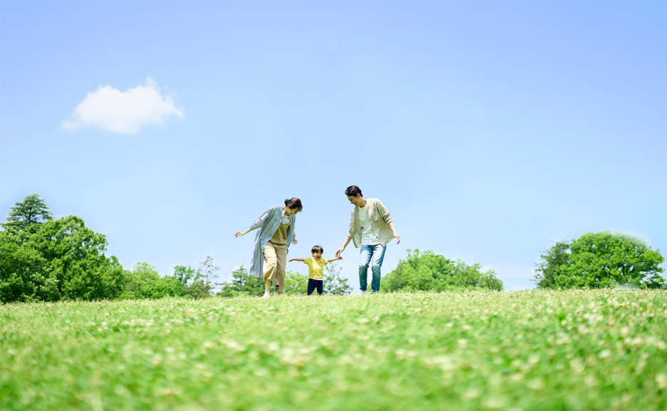 青空と緑豊かな芝生の公園で、子どもとともに過ごす家族の様子