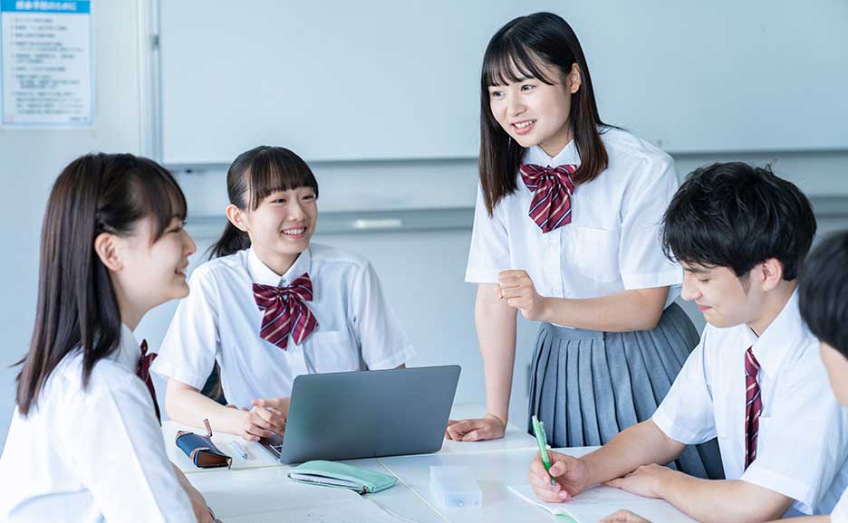 教室で生徒たちが机を囲みノートPCを使いながら話し合う学習風景