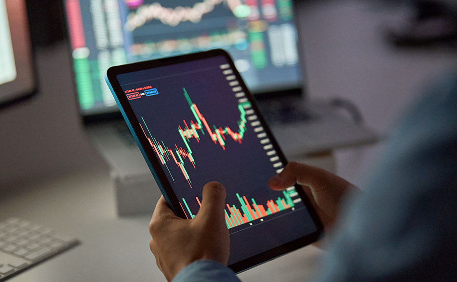 暗い部屋でタブレットとパソコンで株価チャートを見る人