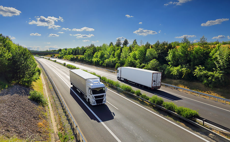 青い空の下、緑豊かな高速道路を走る2台の白い大型トラック