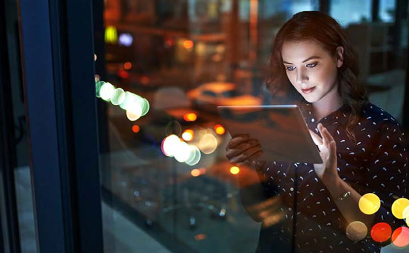 A woman standing next to a window looking at a tablet