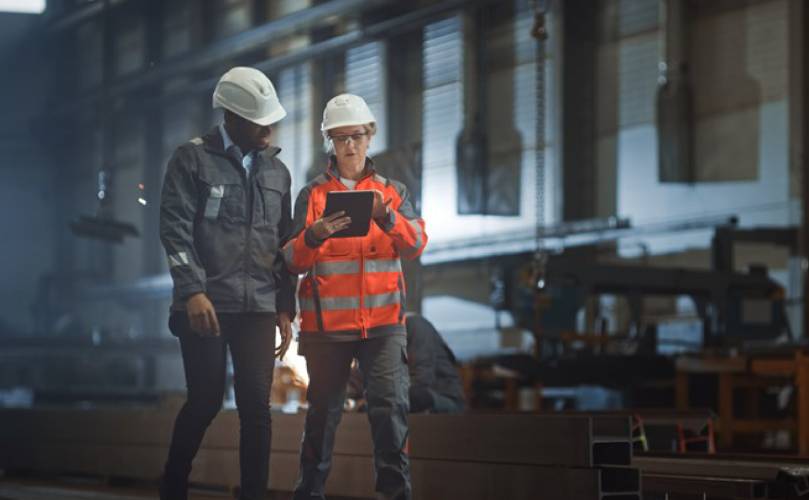 Teammitglieder in Schutzkleidung überprüfen Daten auf einem Tablet im Industriegebiet