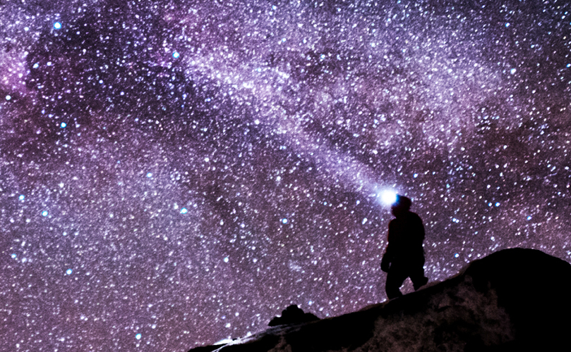 A figure with headlights stands under a starry sky