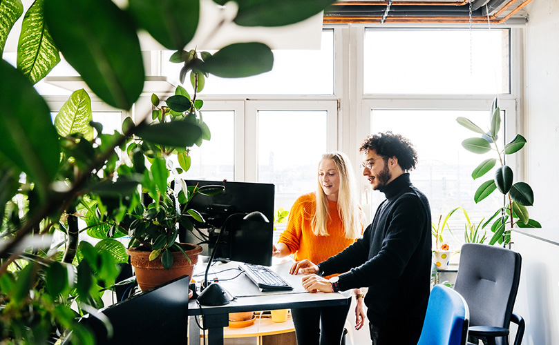 Two person standing at a desk looking at a computer