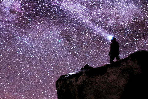 A person standing on a rock wearing a headlamp, with the Milky Way visible in the night sky at Finse.