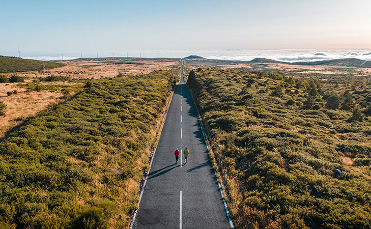 Two people walking on a highland road, wind power generation and the sea in the distance.