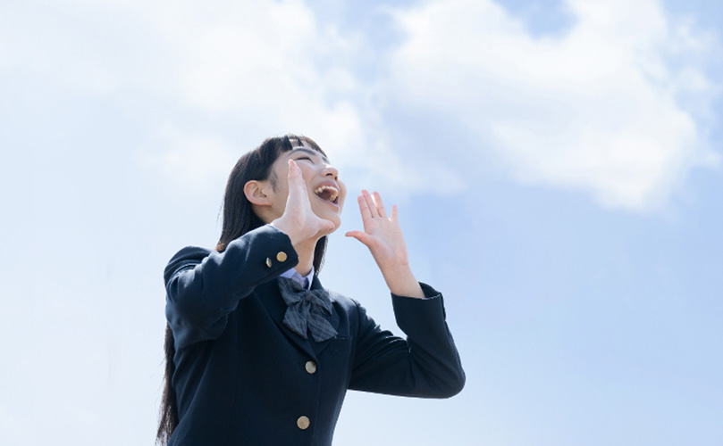 空に向かい笑顔で叫ぶ女子学生