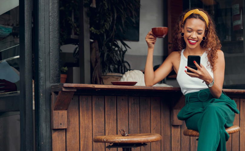 A woman sitting down drinking coffee and laughing at her phone