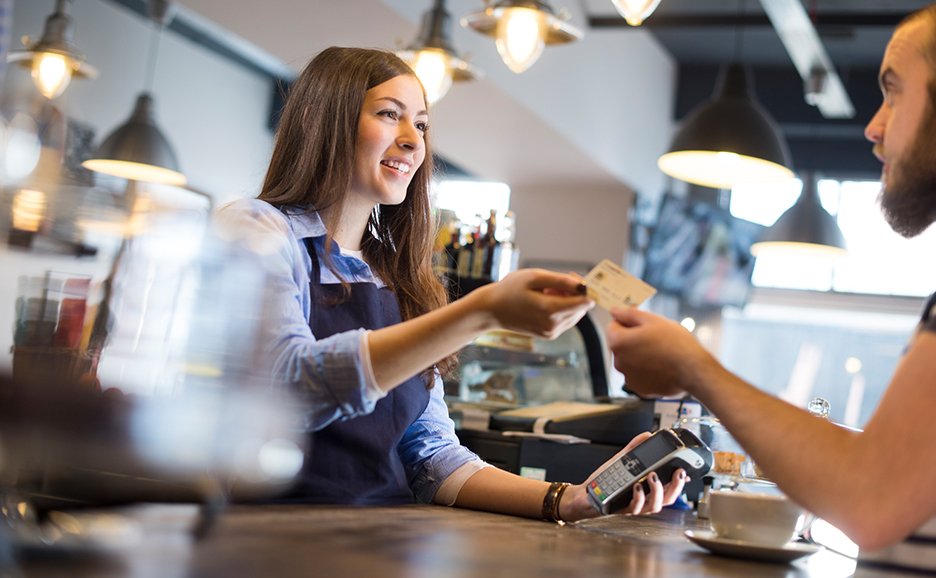 カフェの女性店員がカウンターから男性にクレジットカードを差し出している様子