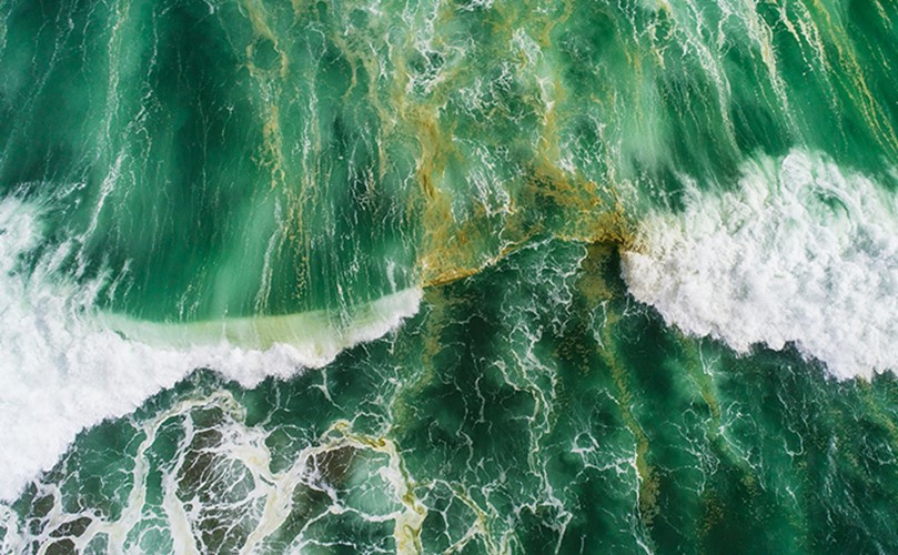 Bird's-eye view of undulating waves in rich green water, capturing the natural beauty and rhythm of the ocean.