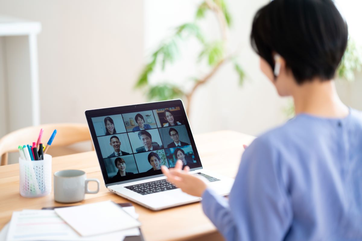 女性社員がオンライン会議で複数の社員に手振りを交えて説明している