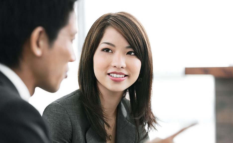 ビジネス環境で会話をしている男女 奥側の女性は笑顔で男性を見ている