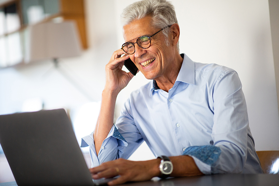 A man makes a phone call while operating a laptop