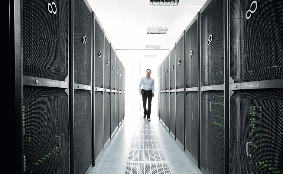 サーバーラックが両側にならぶ通路をこちらに向かって歩く男性