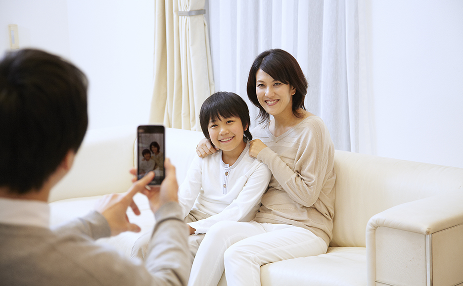 息子と妻が仲良くソファに座っている様子をスマートフォンで撮影する夫