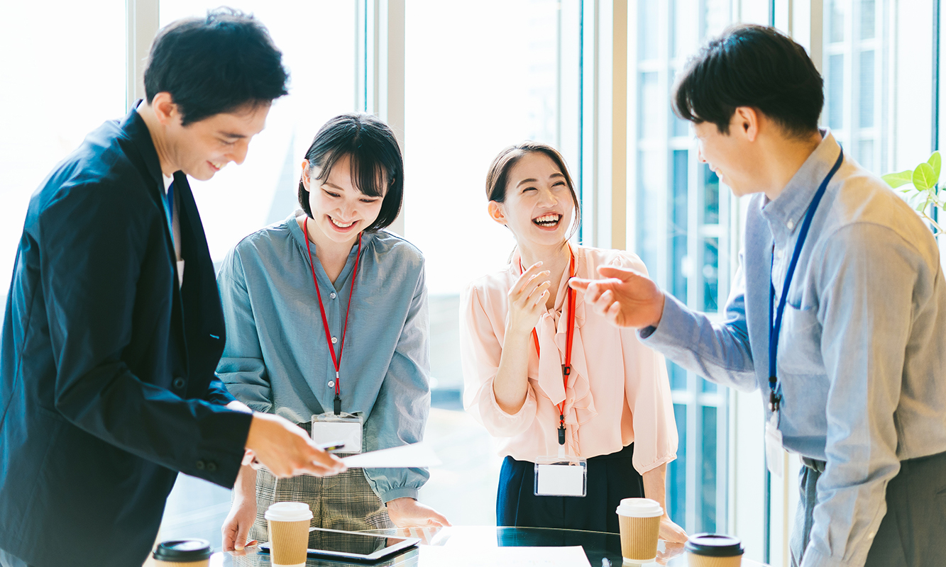 窓際で陽が差す明るいオフィス 和やかに会話する4人のビジネスパーソン
