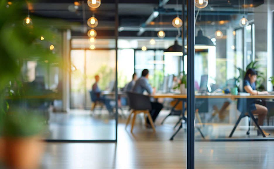 ガラス張りのオフィスで、複数の人がパソコンに向かい業務に集中している様子。