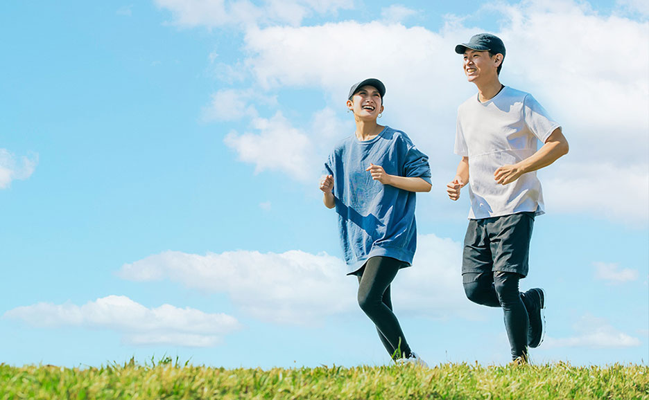 天気の良い日に、青空の下、芝生の上を笑顔で走る若い男女二人組。