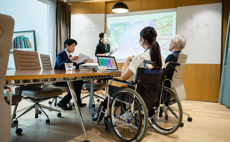 会議中の人々。車椅子に座った女性もいる。
