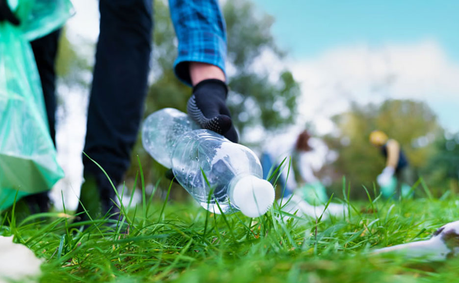 屋外の地面に転がっているペットボトルを、手袋をはめた手が拾い上げている。