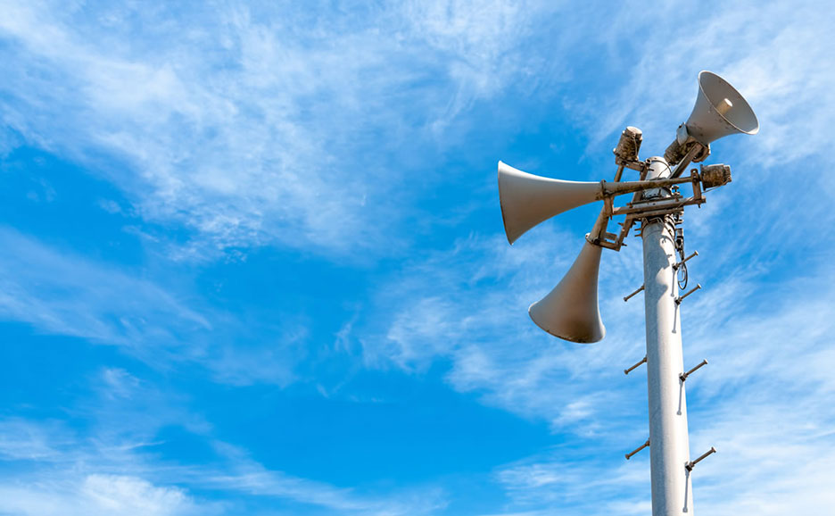 青空に設置された、複数のスピーカーを備えた公共用告知装置。