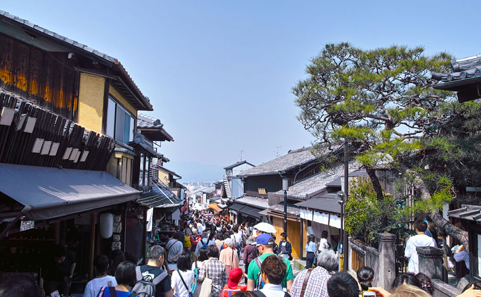 混雑した日本の通りを歩く人々。両脇には伝統的な木造家屋や店が並んでいる