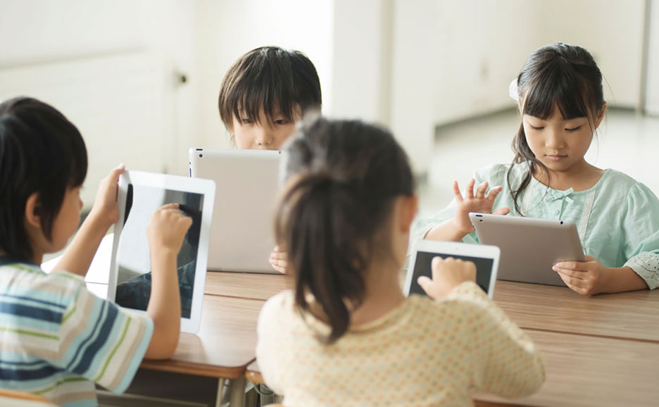 テーブルを囲んで座る子供たちが、それぞれタブレット端末を操作している。