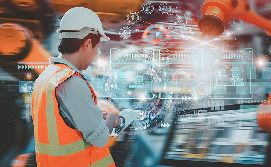 ヘルメットと安全ベストを着用した作業員がタブレットを操作し、工場システムのホログラムが表示されている。