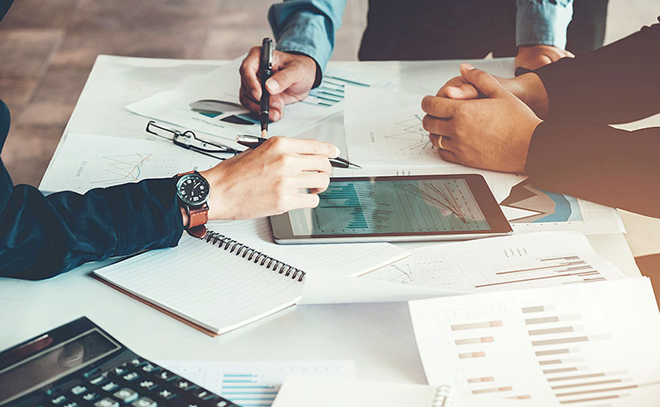 ビジネスパーソンがタブレットと書類を囲んで、データを共有・確認している。