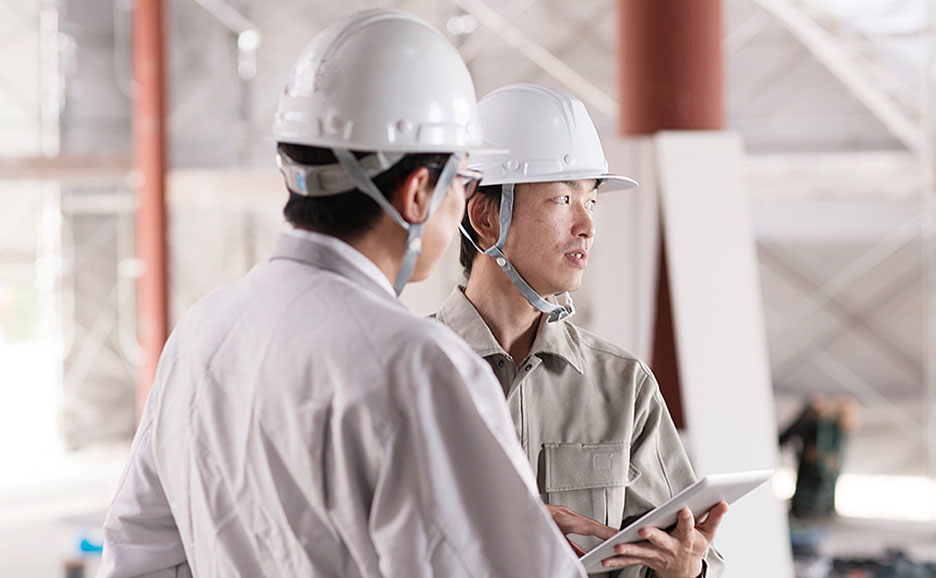 ヘルメットをかぶった男性作業員2名が会話をしている。
