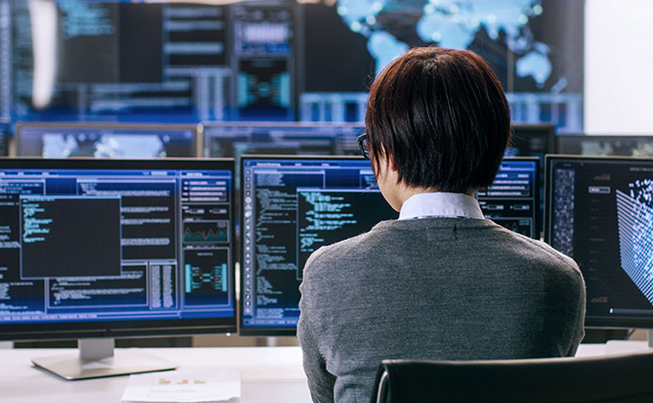 複数のモニター画面と向き合って作業をする情報技術者の後姿