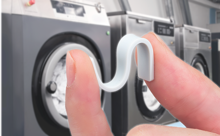 A fingertip holding a FUJITSU RFID linen tag against a backdrop of laundry