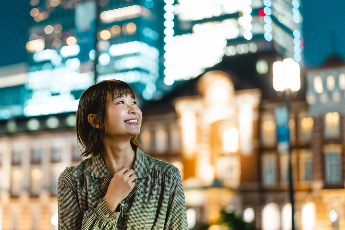 夜の東京駅の前で笑顔でふりあおぐ女性