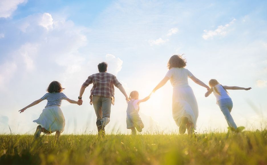 The backs of a family running across the grassland toward the setting sun
