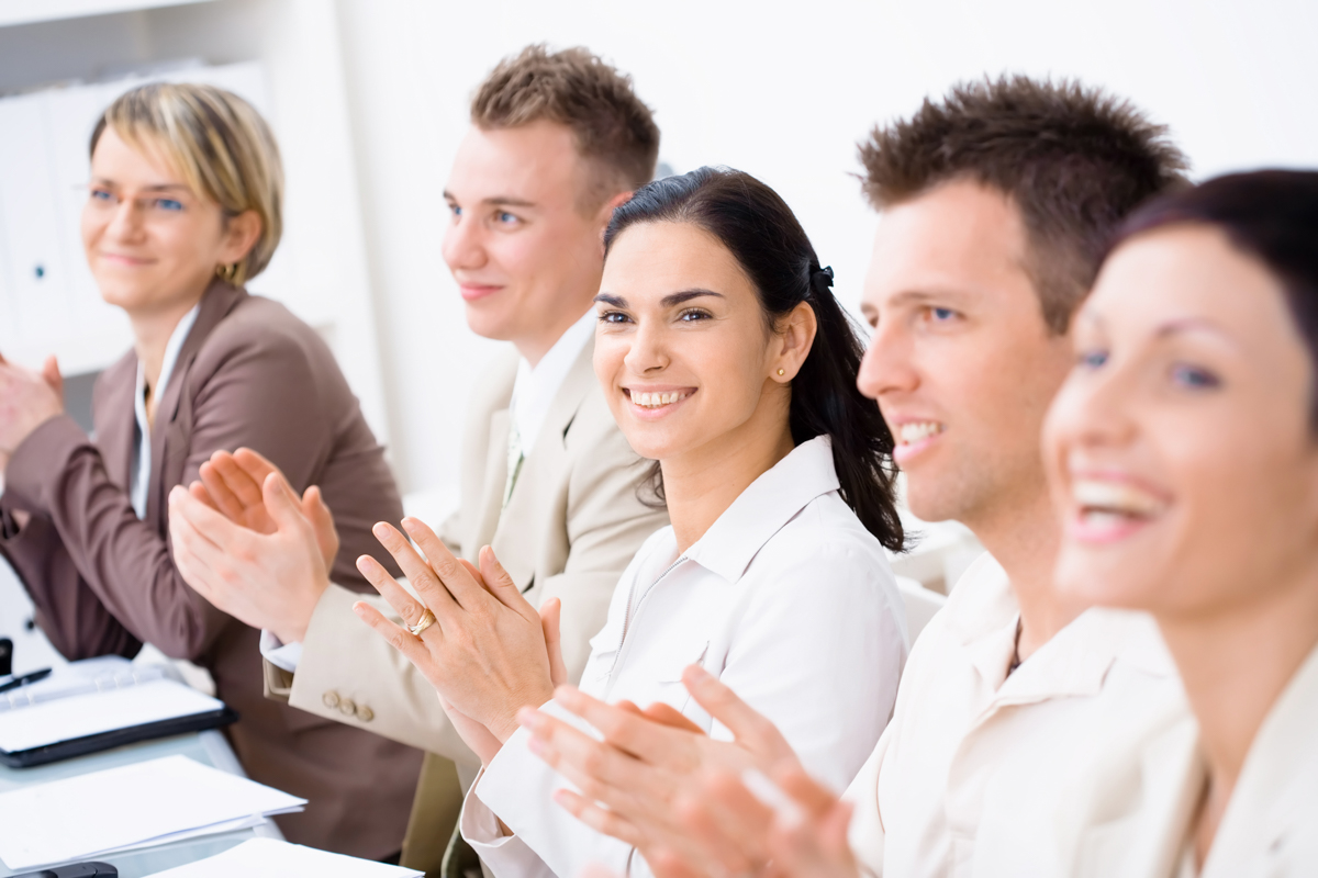 Five business professionals standing in a row, smiling and applauding