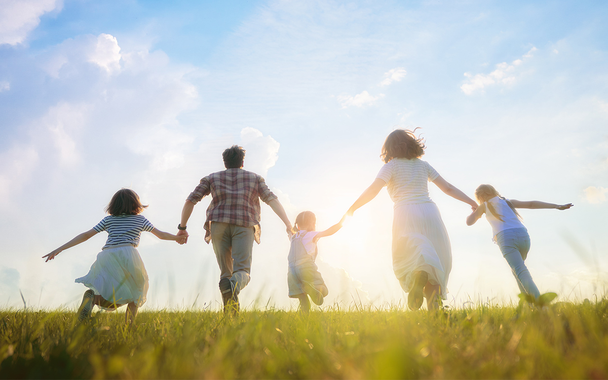 The backs of a family running across the grassland toward the setting sun