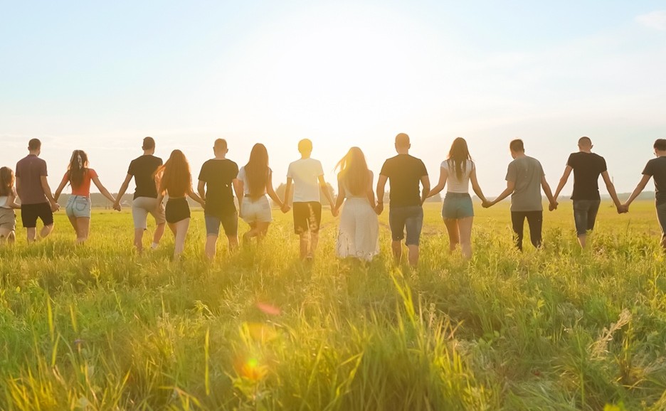 A diverse group of young people holding hands on the grassland, walking toward the setting sun