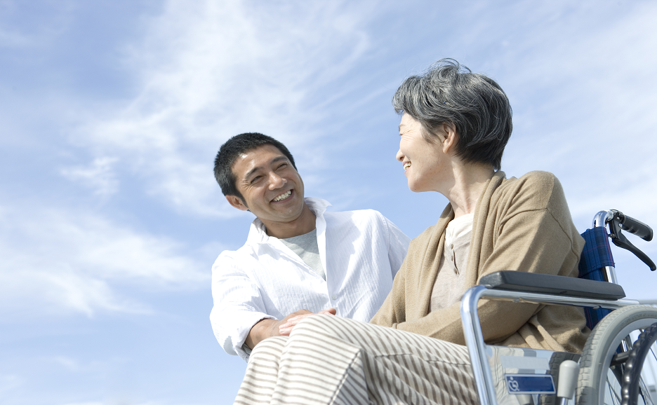 車いすの女性を介助し微笑む男性