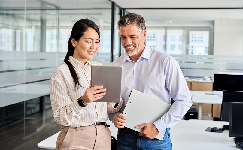 女性がもつタブレットを覗いて満足そうな経営者